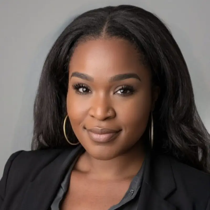 Professional headshot of a woman in black blazer against gray background for dental practice website.