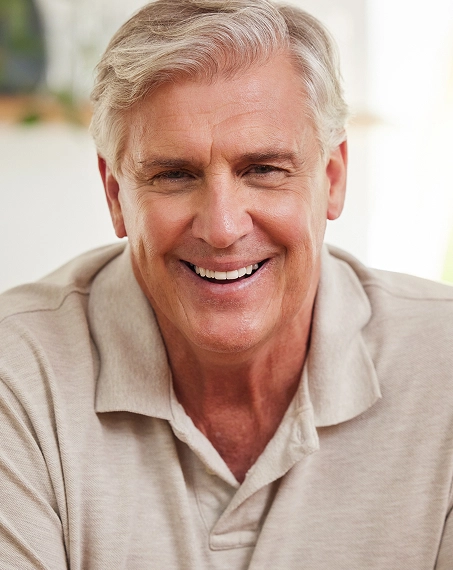 Smiling middle-aged man in tan polo shirt in professional dental office setting.