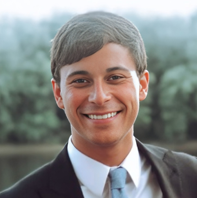 Professional headshot of smiling man in business suit with water and trees in background.