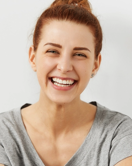 Smiling woman in gray shirt displaying healthy teeth against neutral background.