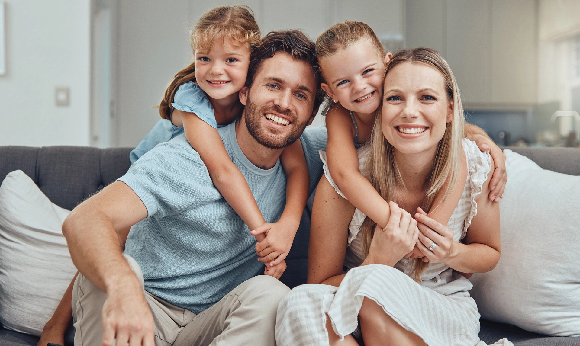 Happy family of four smiling together on couch at home.