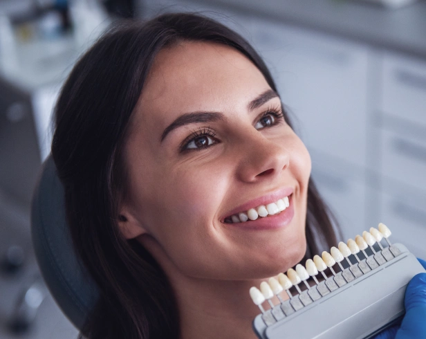 Woman smiling while holding dental shade guide in modern dental office setting.