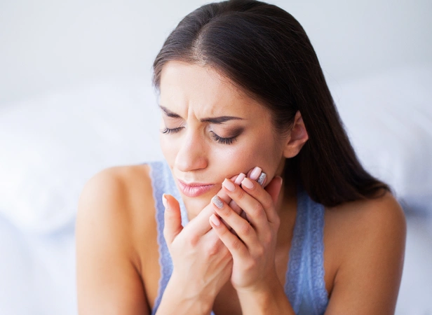 Woman holding face in pain, experiencing tooth sensitivity or dental discomfort indoors.