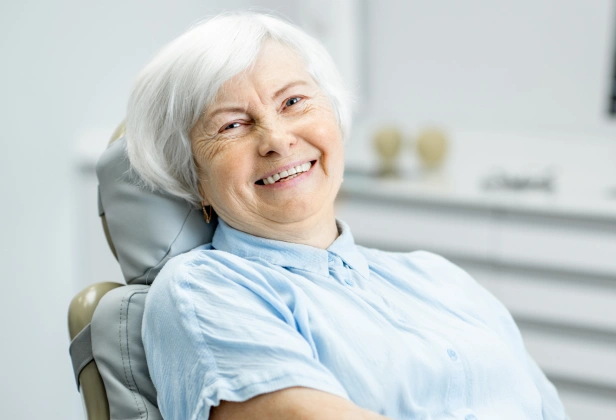 Smiling older woman in dental chair at orthodontic office wearing light blue bib