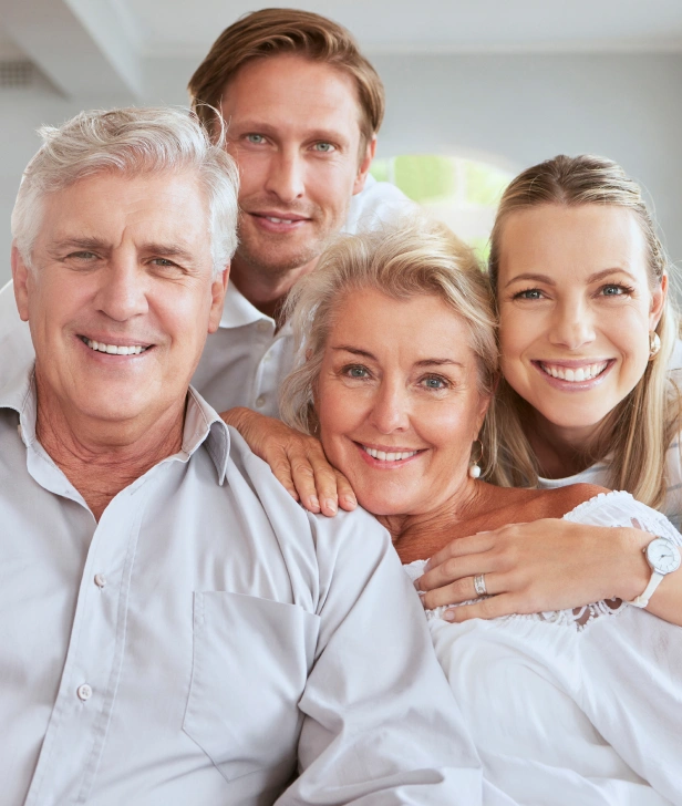 Multi-generational family smiling together indoors in casual white clothing.