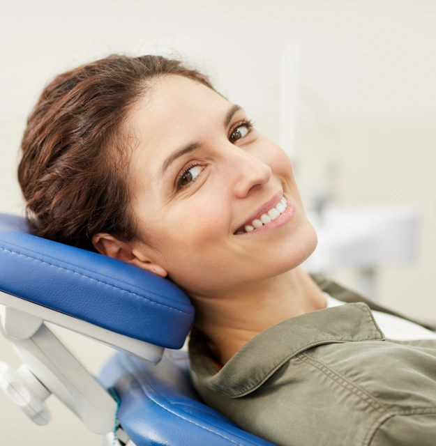 Woman smiling at dental office visit, resting head on blue headrest pillow.