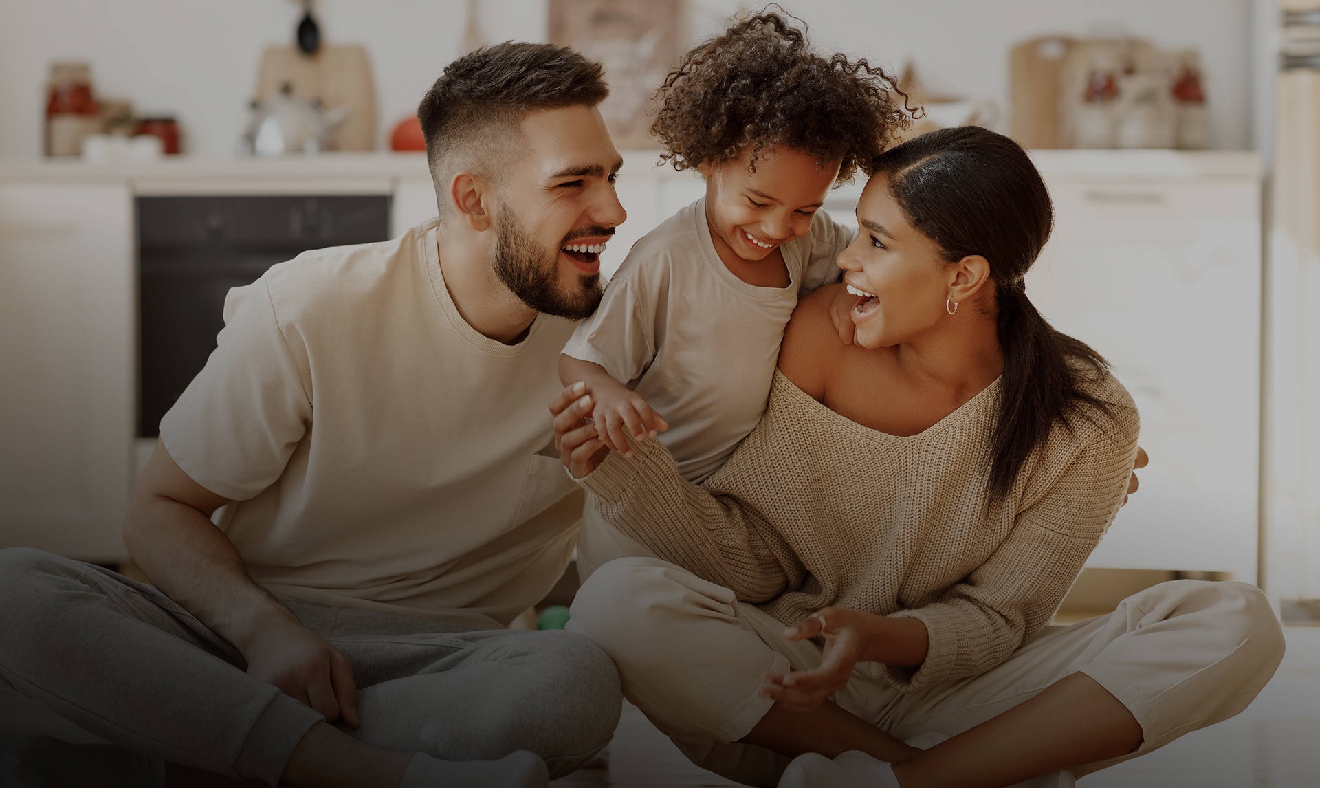 Family of three laughing together on couch in home setting, displaying healthy smiles.