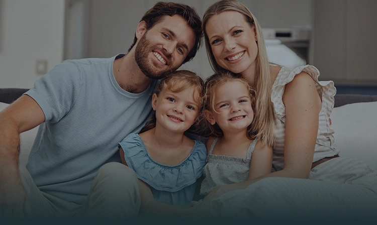 Happy family of four smiling together on couch at home.