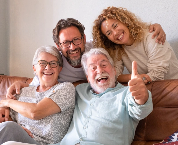 Happy multigenerational family smiling together on couch, representing dental care for all ages.