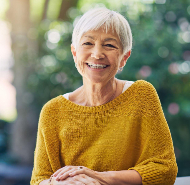 Smiling senior woman in yellow sweater outdoors, representing a confident dental patient.