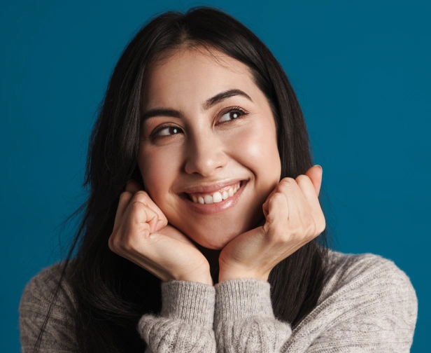 Young woman smiling with hands near face against blue background, dental practice portrait