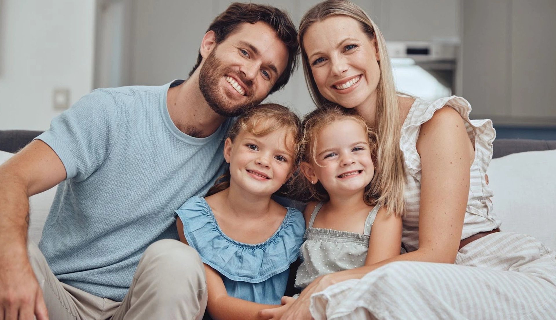 Happy family of four smiling together on bed in home setting.