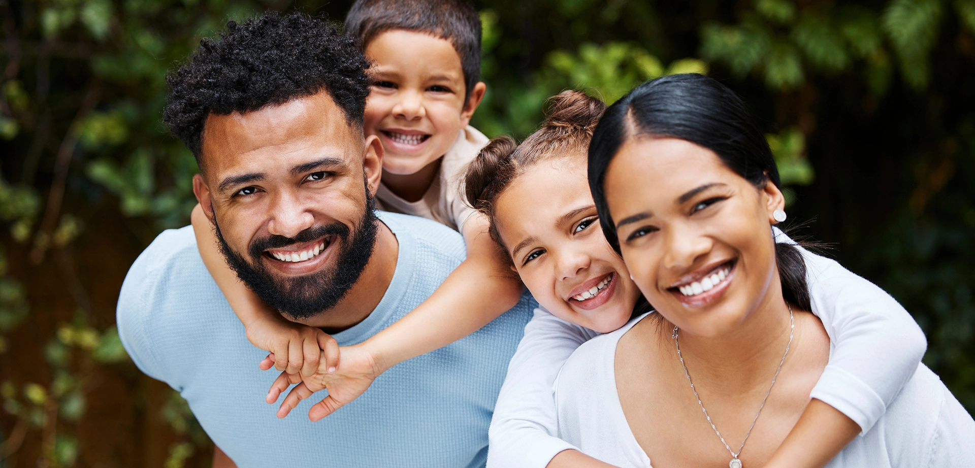 Happy family of four smiling outdoors in nature setting, promoting dental and orthodontics care.