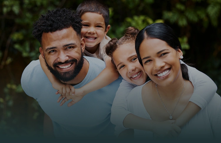 Happy family of four smiling together outdoors with green background