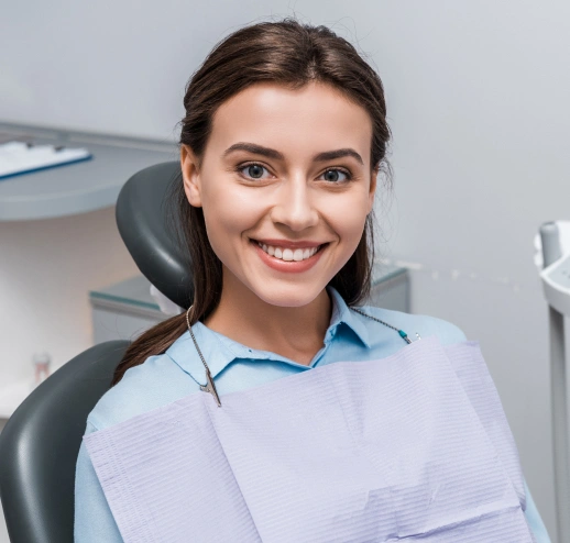 Smiling woman in dental office wearing light blue shirt, seated in dental chair.
