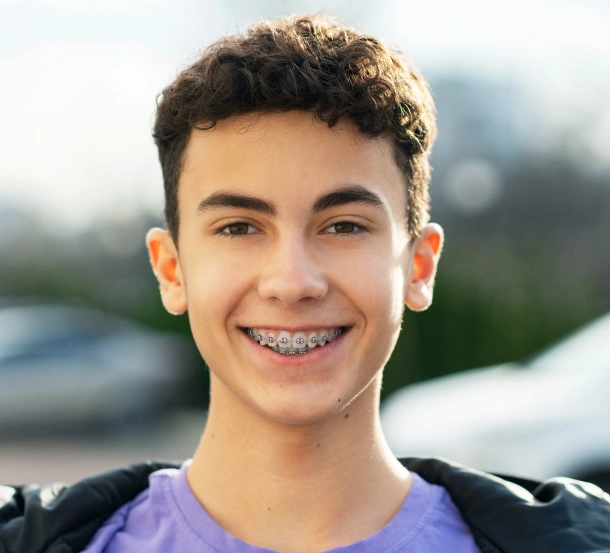 Smiling young boy wearing purple shirt and black jacket outdoors with blurred background