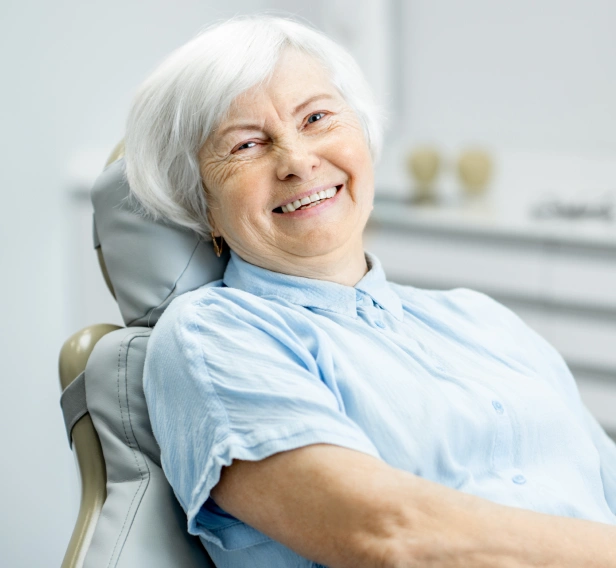 Senior woman smiling in dental chair wearing light blue bib at orthodontics office.