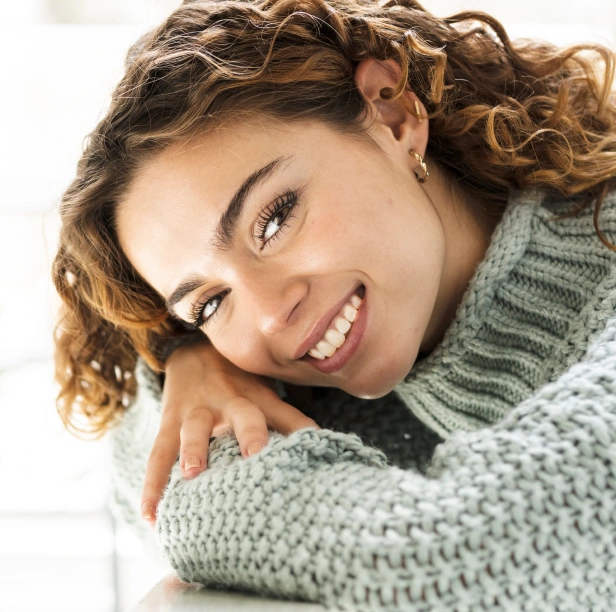 Smiling woman in gray sweater hugging herself against white background for dental practice.