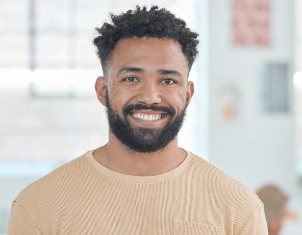 Smiling man in beige shirt at dental office with blurred background