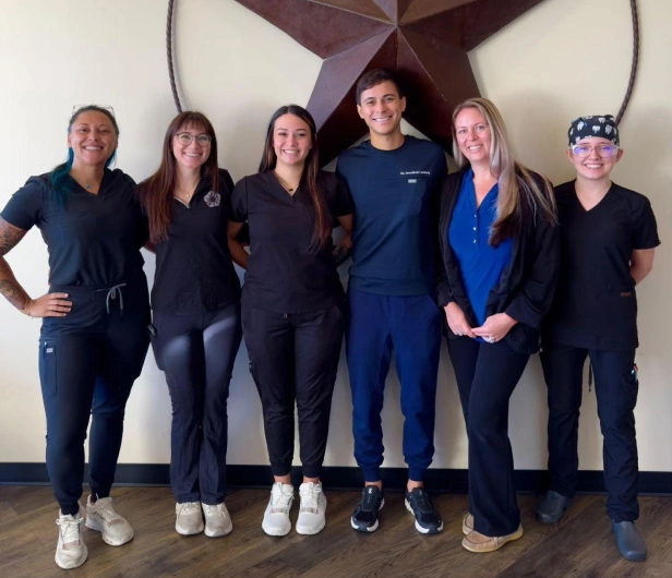 Six dental team members standing together in front of a geometric star design on wall.