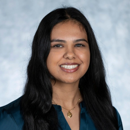 Professional headshot of smiling woman with long dark hair against blurred background for dental practice.