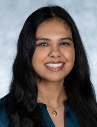 Professional headshot of a smiling woman with long dark hair against a light blue background.