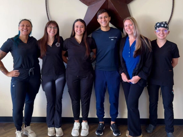 Six dental team members in blue and black scrubs stand together in front of a star logo.