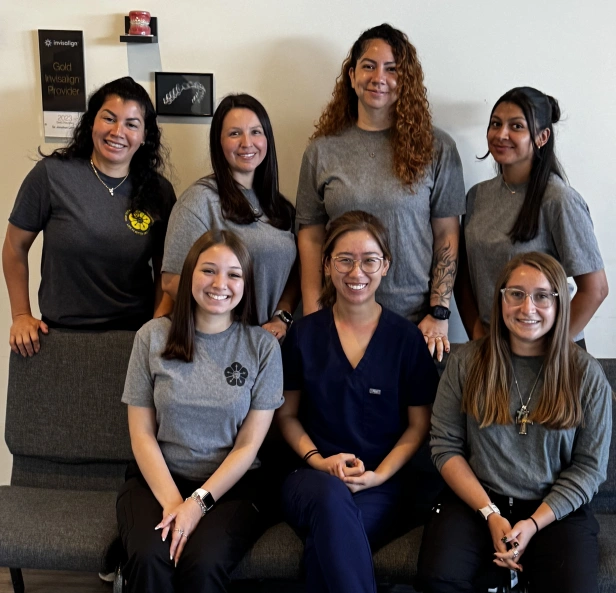 Dental team of seven women smiling together in office setting with wall decorations.