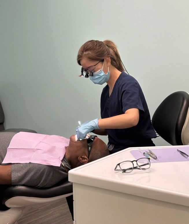 Dental professional wearing mask examines patient's teeth in clinical treatment room.