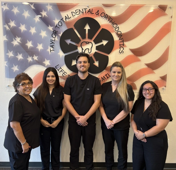 Five dental professionals in black scrubs stand together against American flag backdrop with practice logo.