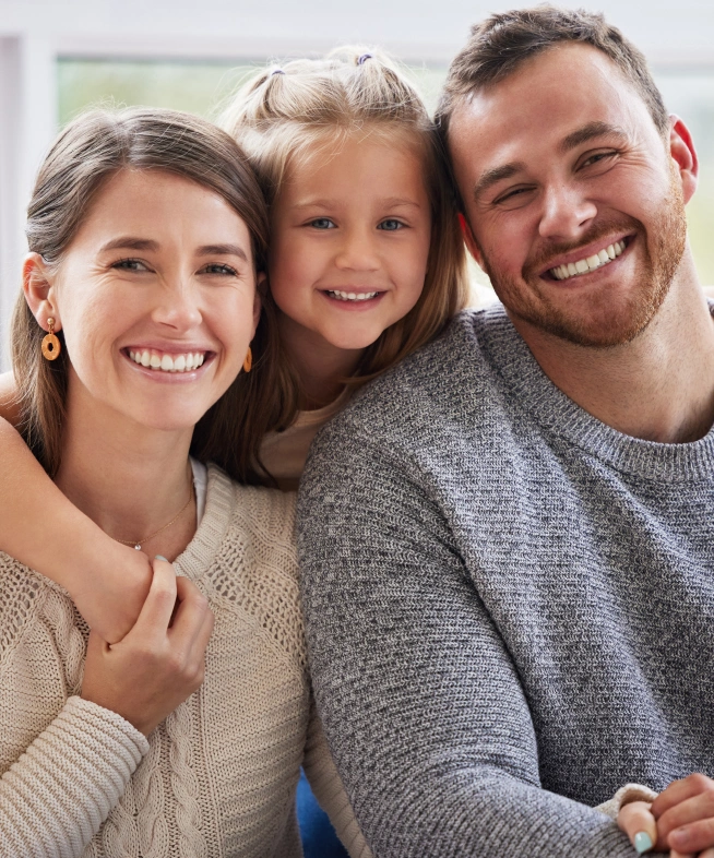 Happy family of three smiling together indoors, promoting dental and orthodontics care.