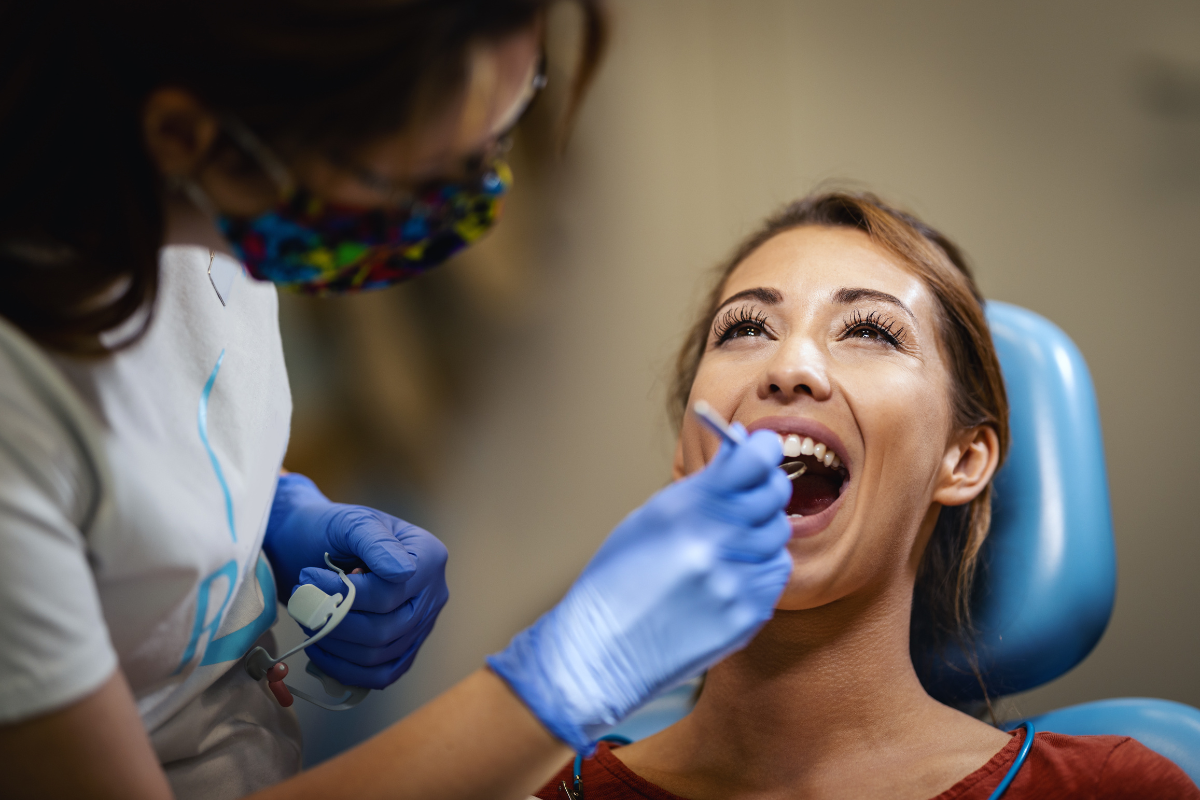 Dentist in blue gloves examining patient's teeth in dental chair during checkup.