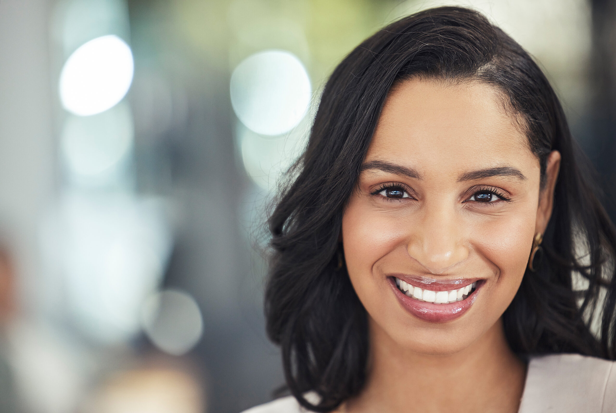 Professional woman smiling at camera in modern dental office setting with blurred background.