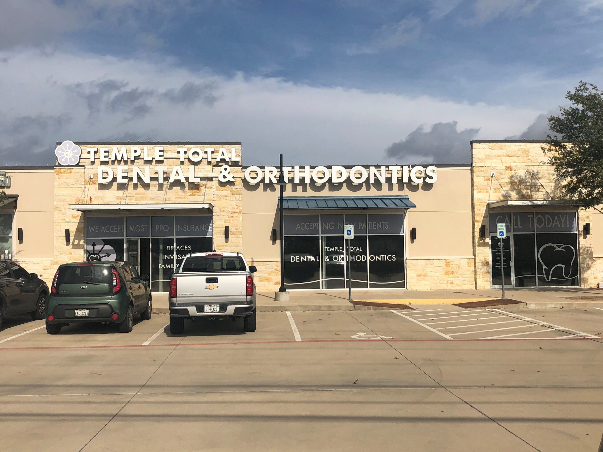 Dental orthodontics office storefront with parking lot and vehicles during daytime.